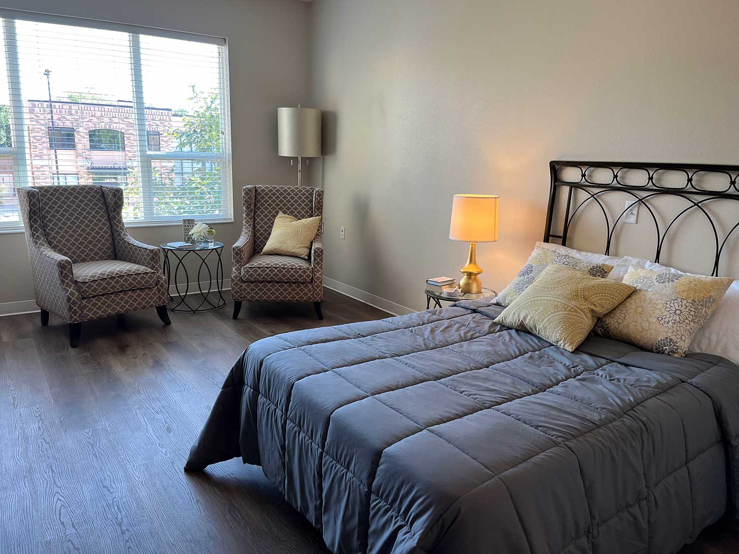 The Rosemount, care suites view with window, bed and chairs, table and reading lamp, sunny view beyond window with trees and nearby buildings